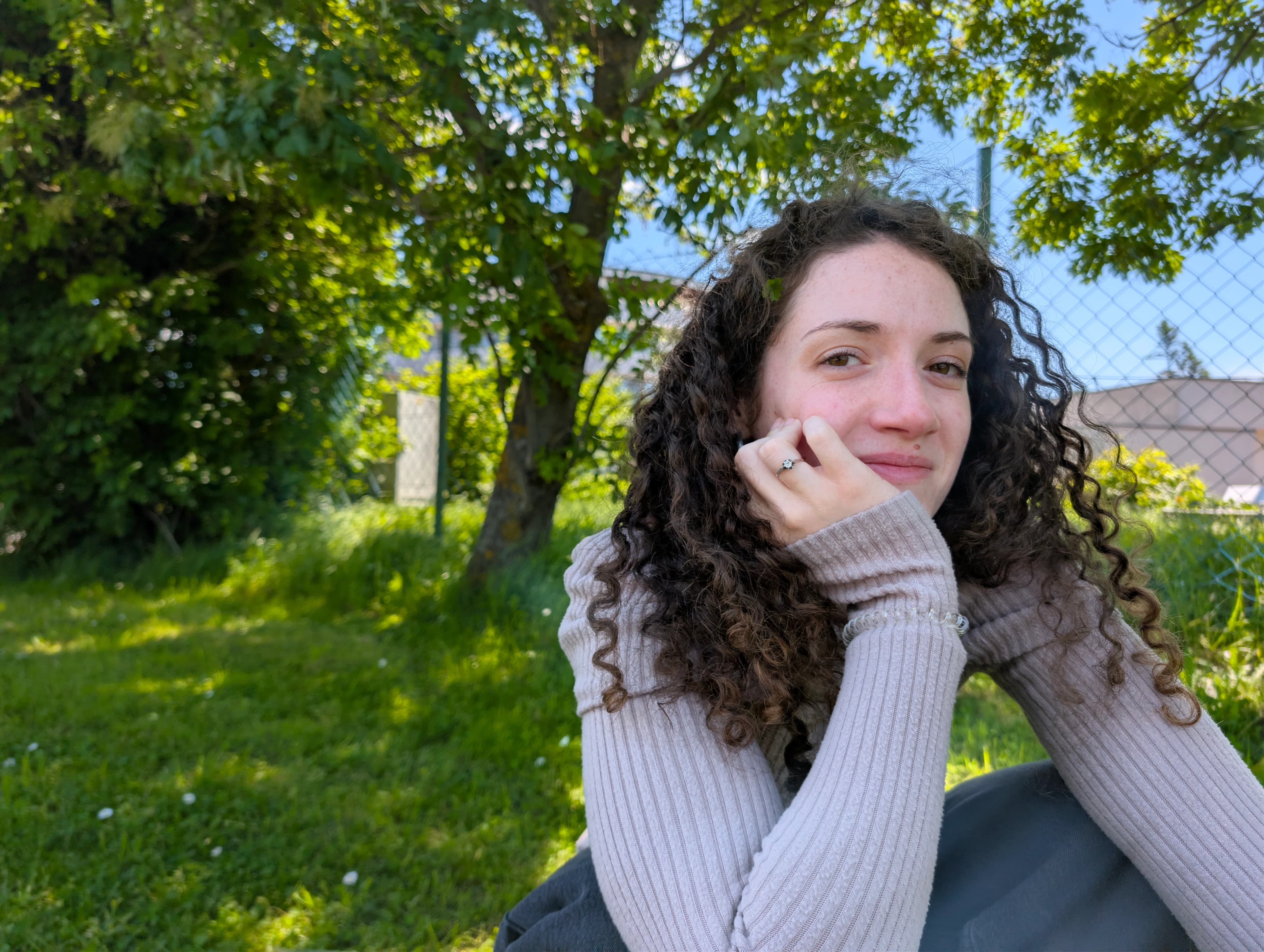 Dóra sitting in the grass under a tree, chin resting on her hand